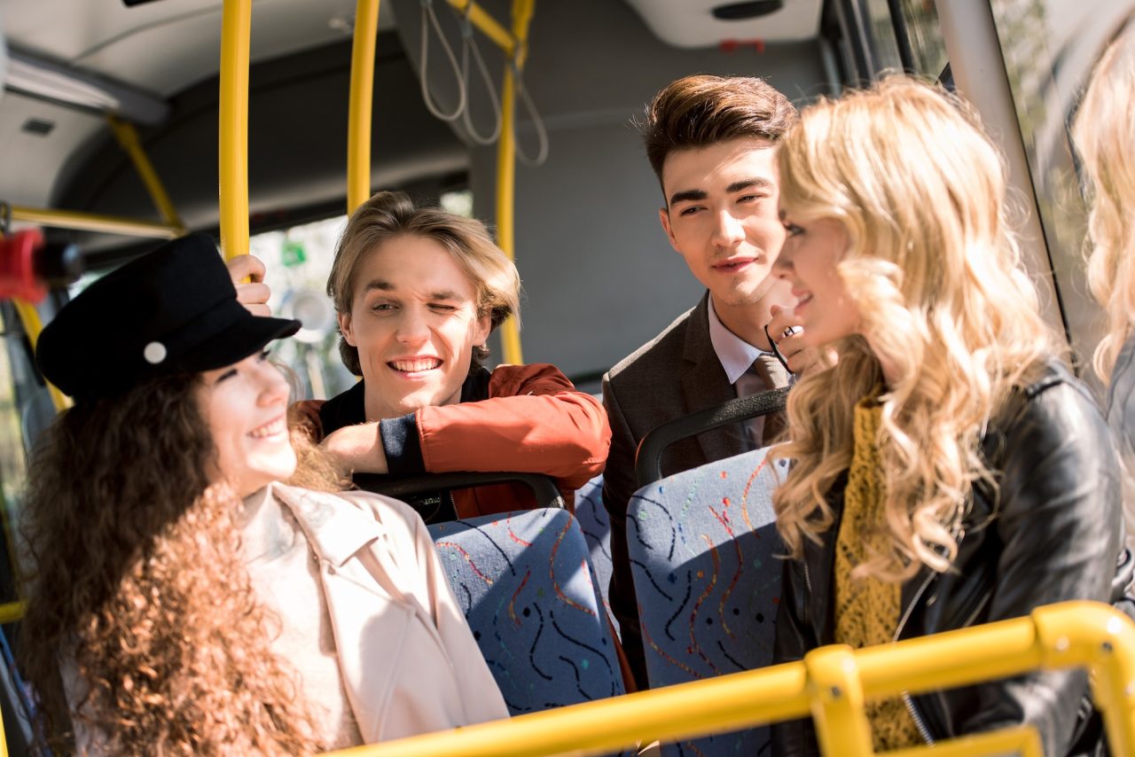 happy young friends talking while sitting in city bus